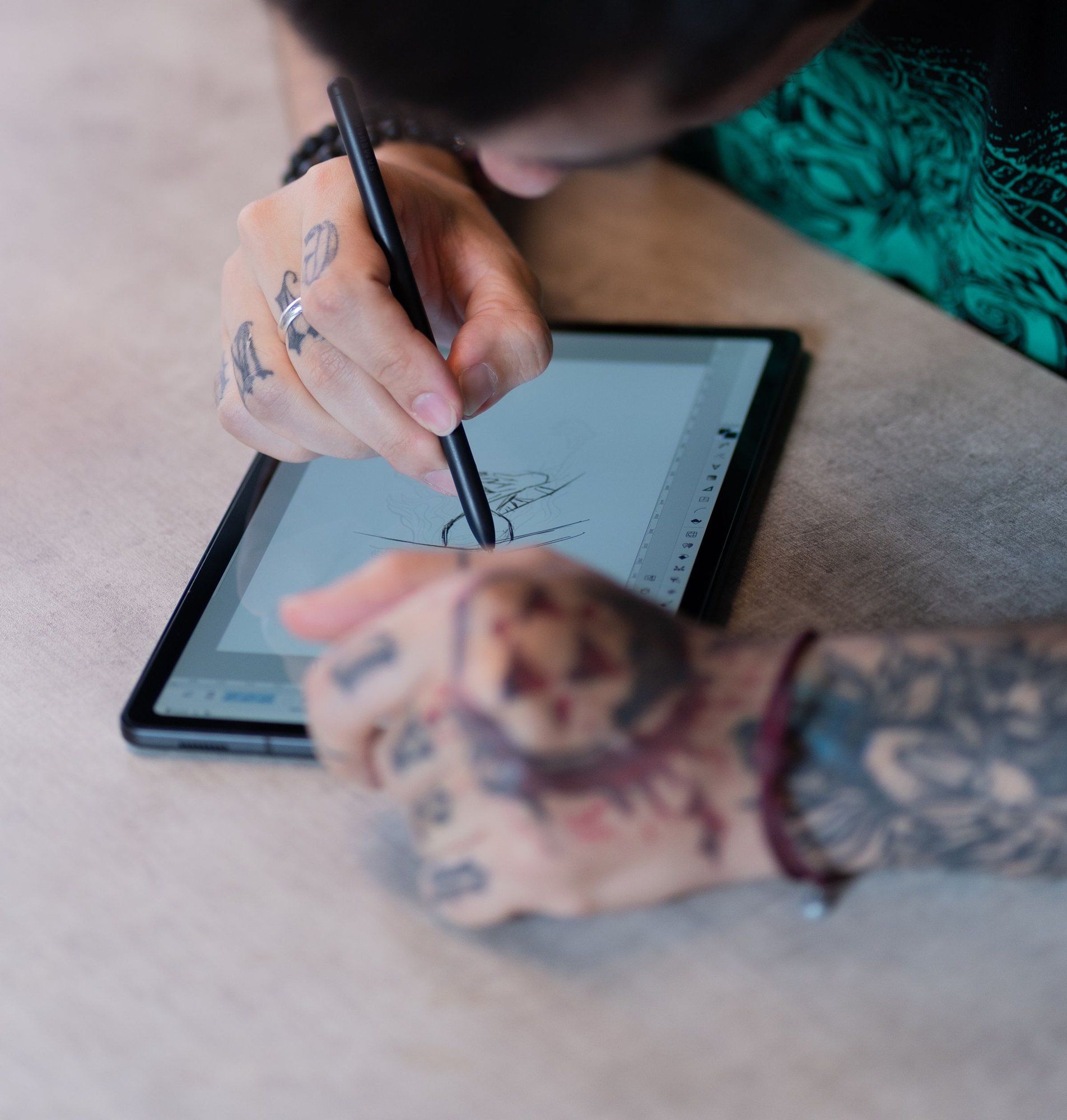Eine tätowierte Hand zeichnet mit dem Stift einen Entwurf auf einem Tablet