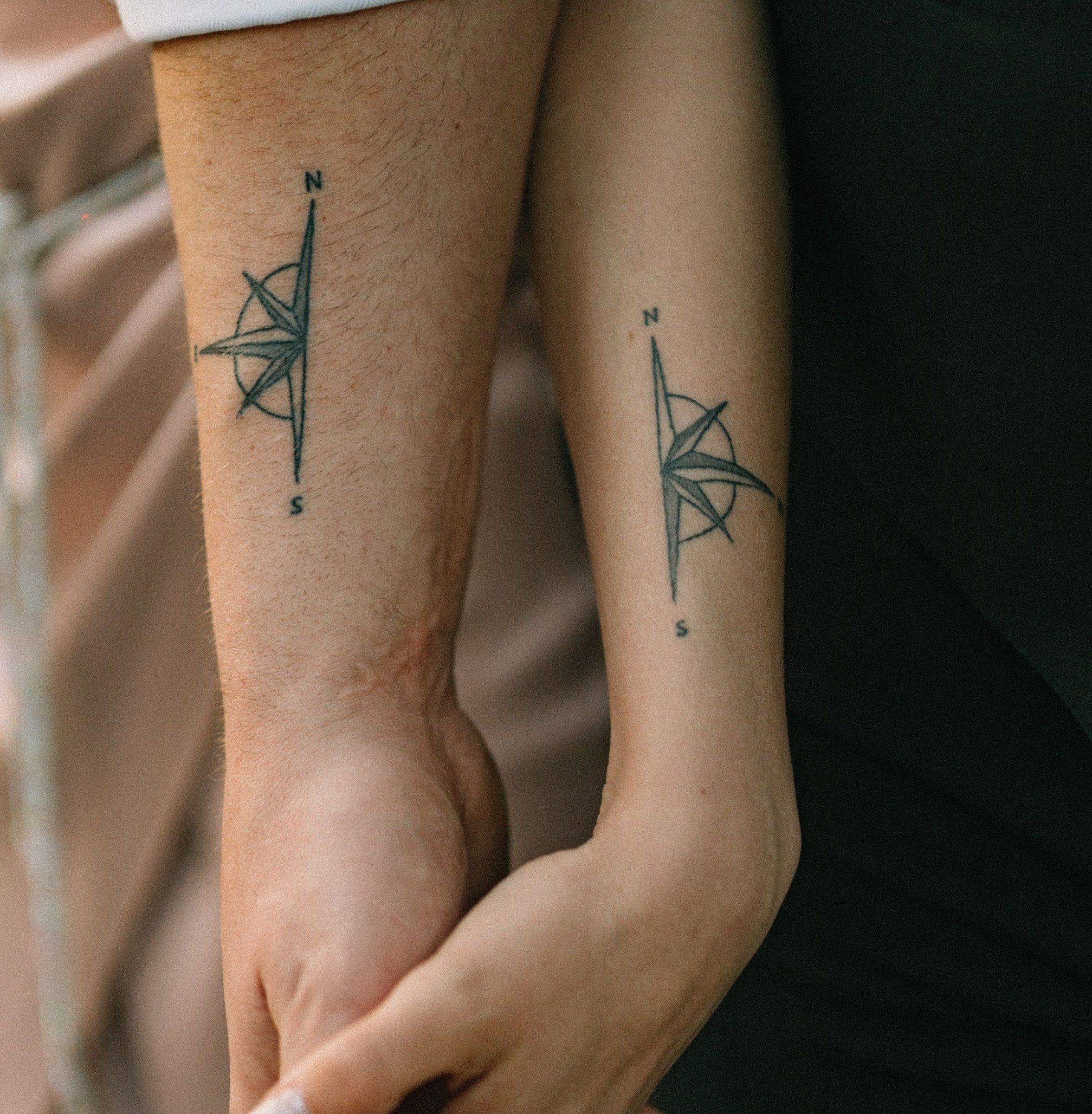 Zwei Unterarme nebeneinander, auf jedem eine kleine Kompassrose in feinen Linien