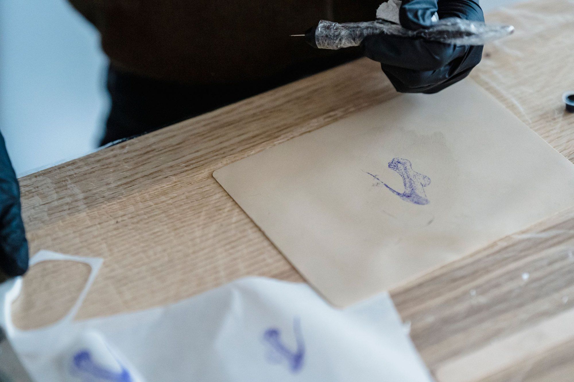Schablonenpapier mit einer violetten Zeichnung auf einem Holztisch, daneben eine Hand im Handschuh