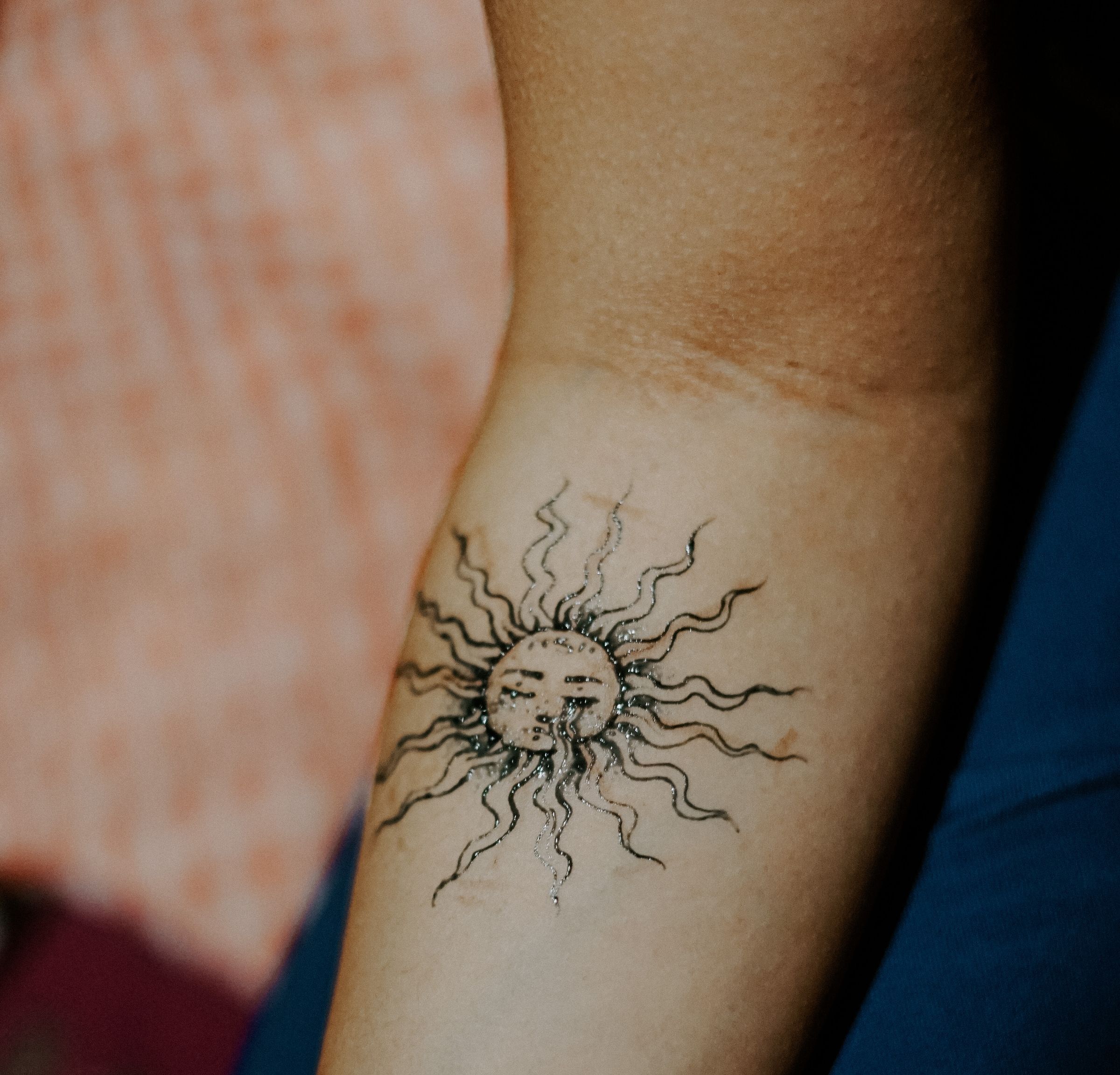 Unterarm mit einer Sonne mit geschwungenen Strahlen in schwarzen Konturen
